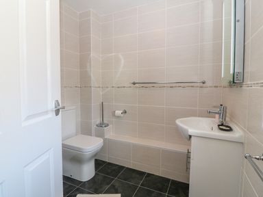 A bathroom with a toilet and sink against tiled walls at Gwynlys in Cemaes Bay