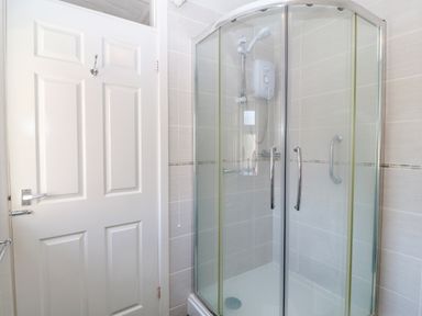 A bathroom with a glass shower enclosure and a white door at Gwynlys in Cemaes Bay