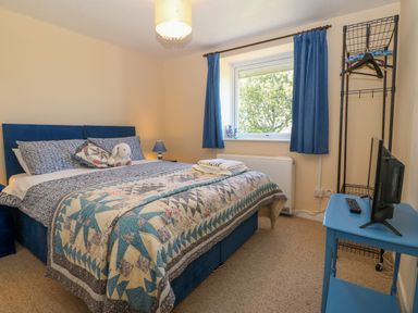 A bedroom with a double bed a quilt blue curtains a small blue table with a TV and a metal clothes rack at Gwynlys in Cemaes Bay