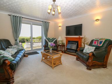 A living room with leather sofas a glass coffee table a fireplace and sliding glass doors at Gwynlys in Cemaes Bay