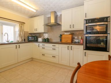A kitchen with white cabinets brown countertops a double oven a microwave a toaster and a wooden table at Gwynlys in Cemaes Bay