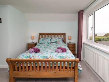 A bedroom with a wooden double bed with floral bedding and rolled towels on top at Carousel in Broad Haven