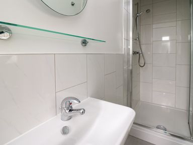 A bathroom with a white sink and chrome faucet and a glass enclosed shower at Carousel in Broad Haven
