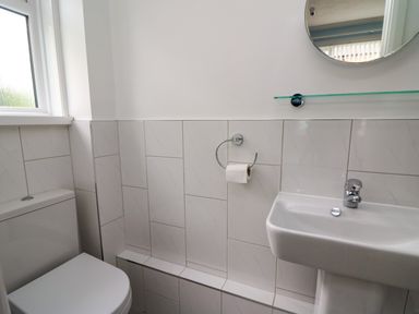 A small bathroom with a toilet a sink a round mirror and a window at Carousel in Broad Haven