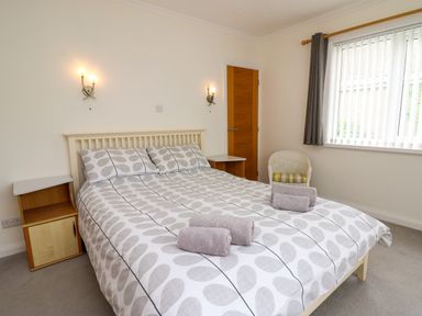 A bedroom with a double bed two bedside tables a chair and a window with blinds at Carousel in Broad Haven