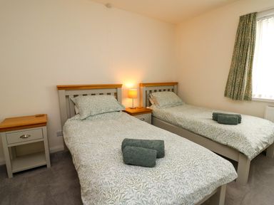 A bedroom with two single beds bedside tables lamp and a window with curtains at Carousel in Broad Haven