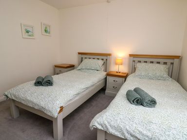 A bedroom with two single beds with patterned bedding and rolled towels on each bed at Carousel in Broad Haven