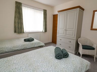 A bedroom with two single beds each with rolled towels floral curtains a wardrobe and a wicker chair at Carousel in Broad Haven