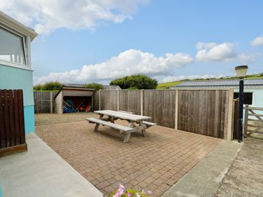 An outdoor patio area with a wooden picnic table a lamp post a shed with garden items and a wooden fence at Carousel in Broad Haven