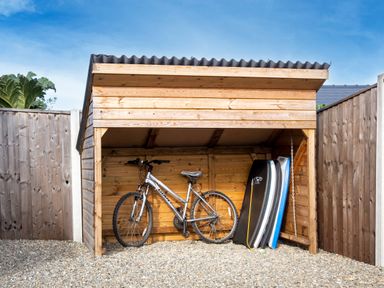 A wooden outdoor shed with a bicycle and bodyboards inside at Carousel in Broad Haven