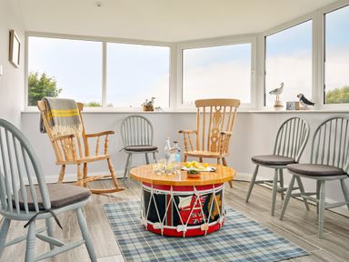 A sitting area with wooden and painted chairs around a drum table with drinks on a checkered rug at Carousel in Broad Haven