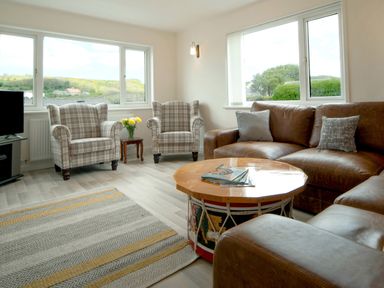 A living room with leather sofa two plaid armchairs a drum shaped wooden coffee table and a patterned rug at Carousel in Broad Haven