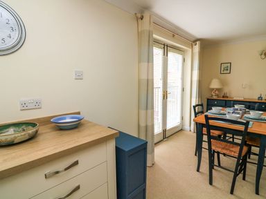 A dining area with a wooden table set with bowls and cups next to glass doors with blinds at 8 Dartmouth House in Dartmouth
