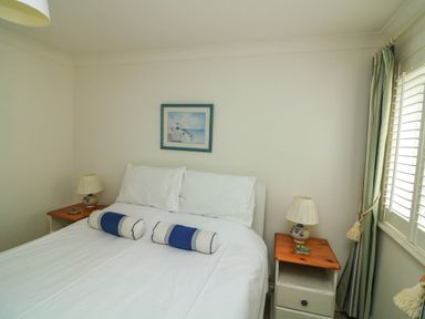 A bedroom with a bed with white bedding and two blue and white cushions with two nightstands each with a lamp and a painting on the wall at 8 Dartmouth House in Dartmouth
