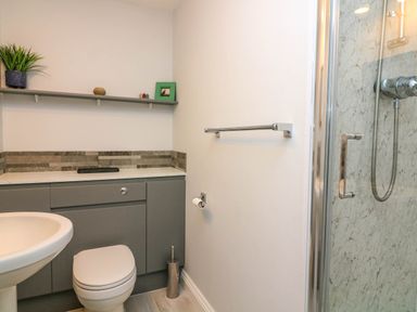 A bathroom with a toilet sink shower and gray cabinets with a shelf holding decorations at 8 Dartmouth House in Dartmouth
