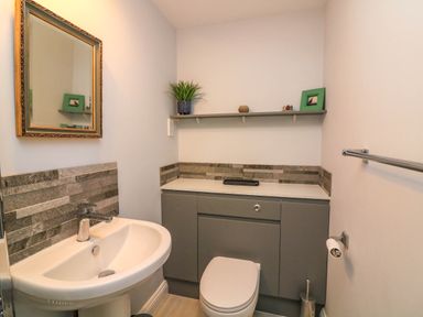 A bathroom with a pedestal sink and mirror above it a toilet with cabinet behind it and a shelf with decorative items at 8 Dartmouth House in Dartmouth