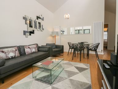 A living room with a black sofa and armchair a glass coffee table and a dining table with black chairs at 12 Blue Hill Park Ambleside