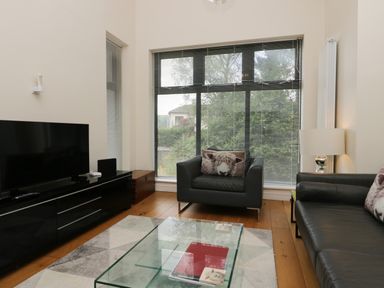 A living room with black leather furniture a glass coffee table and a large window at 12 Blue Hill Park in Ambleside
