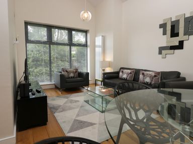 A living room with black leather sofas with sheep cushions a glass coffee table and a large window at 12 Blue Hill Park in Ambleside