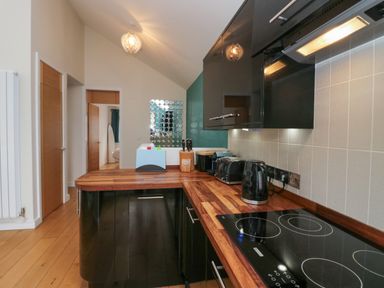 A kitchen with wooden countertops black cabinets an electric stovetop and various appliances at 12 Blue Hill Park in Ambleside
