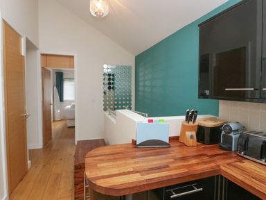 A kitchen counter with knives toaster and coffee machine and a hallway leading to a bedroom at 12 Blue Hill Park in Ambleside