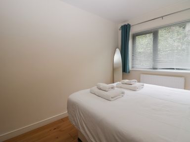 A bedroom with a white bedspread and folded towels on the bed next to a window with blinds and curtains at 12 Blue Hill Park in Ambleside