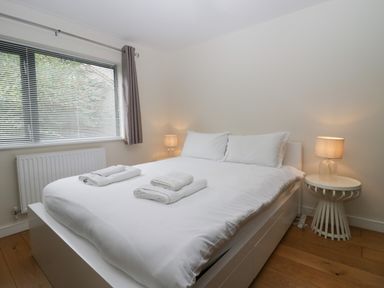 A bedroom with a white bed with towels on it a bedside table with a lamp and a window with blinds at 12 Blue Hill Park in Ambleside