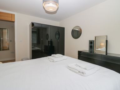 A bedroom with a bed folded towels on it a black wardrobe a black dresser with mirrors and a ceiling light fixture at 12 Blue Hill Park in Ambleside