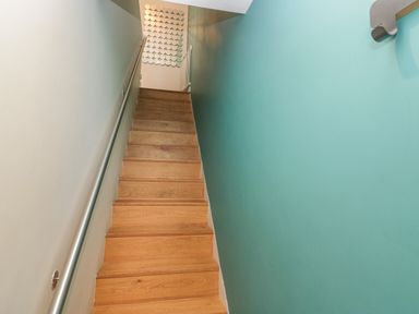 A wooden staircase with a metal handrail and a teal wall on the right at 12 Blue Hill Park in Ambleside