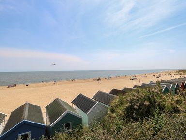 A beach with colorful beach huts and people on the sand at Iona Cottage Southwold