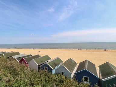 A view of beach huts with a sandy beach and sea at Iona Cottage in Southwold