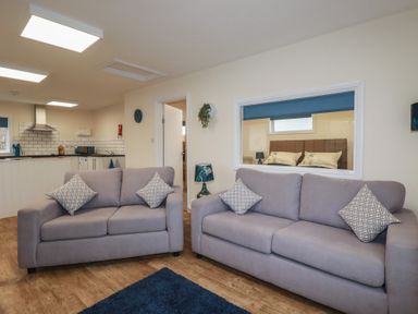 A living room with two sofas and cushions with a view into a kitchen and bedroom at Kingfisher Lodge in Treverbyn near St Austell