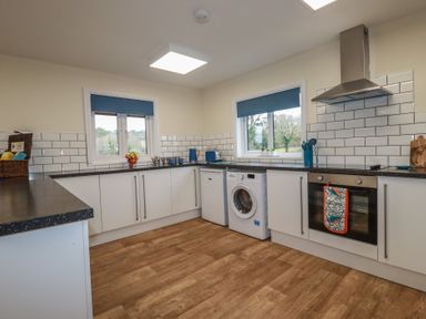 A kitchen with white cabinets two windows a washing machine oven and wooden floor at Kingfisher Lodge in Treverbyn near St Austell