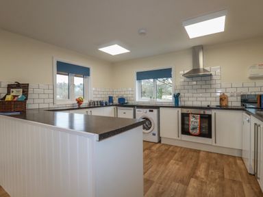 A kitchen with white cabinets a washing machine an oven and windows with blue blinds at Kingfisher Lodge in Treverbyn near St Austell