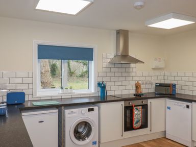 A kitchen with a washing machine oven fridge microwave toaster and utensils with a window showing trees at Kingfisher Lodge in Treverbyn near St Austell