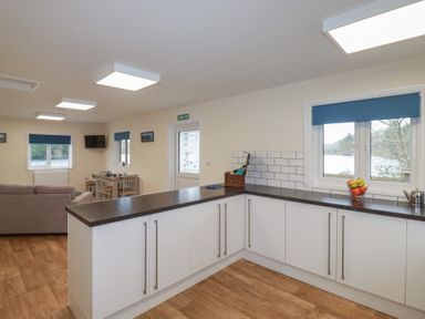 A kitchen with white cabinets and black countertop next to a dining area and living room at Kingfisher Lodge in Treverbyn near St Austell
