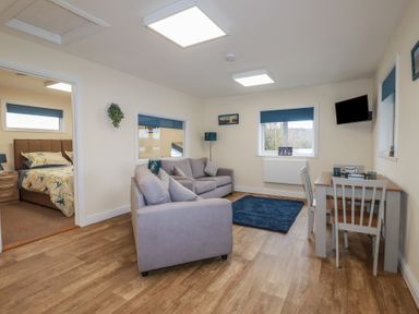 A living room with two sofas a small dining table and chairs and a bedroom visible through an open door at Kingfisher Lodge Treverbyn near St Austell