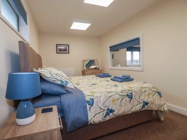 A bedroom with a double bed a nightstand with a lamp a chest of drawers with a mirror and folded towels on the bed at Kingfisher Lodge Treverbyn near St Austell