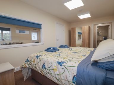 A bedroom with a double bed blue and floral bedding towels on bed wooden wardrobe and window looking into another room at Kingfisher Lodge in Treverbyn near St Austell
