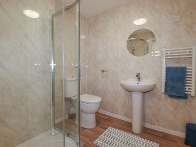 A bathroom with a shower enclosure toilet pedestal sink round mirror and towel rail at Kingfisher Lodge in Treverbyn near St Austell