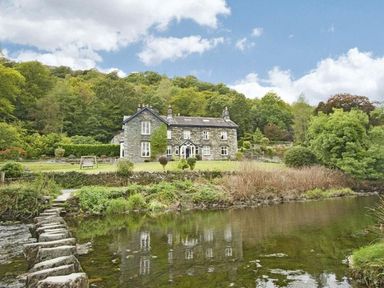A stone house near a river with a stepping stone path and trees at Riverbank At Stepping Stones in Rydal