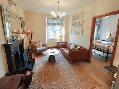 A living room with a brown leather sofa armchair round coffee table and a window with floral blinds at Riverbank At Stepping Stones in Rydal