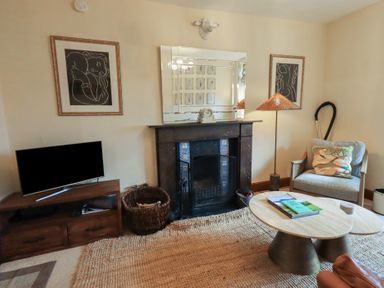 A living room with a fireplace TV table armchair coffee tables and framed artwork at Riverbank At Stepping Stones in Rydal