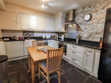 A kitchen with wooden table and chairs stone wall clock appliances and white cabinets at Riverbank At Stepping Stones in Rydal