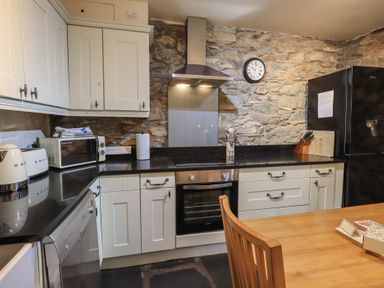 A kitchen with white cabinets a black countertop stone walls and a wooden dining table at Riverbank At Stepping Stones in Rydal
