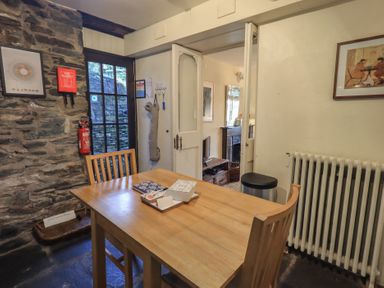 A dining area with a wooden table and two chairs near a stone wall and a door leading to another room at Riverbank At Stepping Stones in Rydal