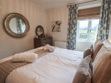 A bedroom with a bed pillows rolled towels a dresser with two round mirrors and curtains at Riverbank At Stepping Stones in Rydal