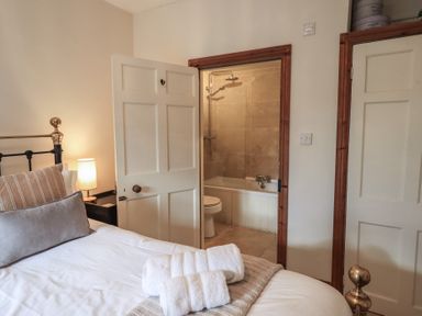 A bedroom with a brass bed and folded towels on the bed showing an open door to a bathroom with a shower and bathtub at Riverbank At Stepping Stones in Rydal