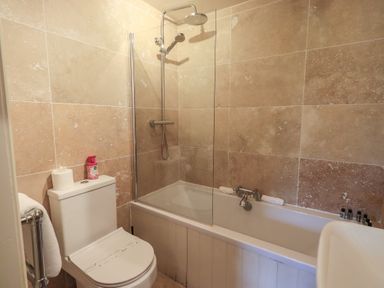 A bathroom with a toilet a bathtub with shower and toiletries at Riverbank At Stepping Stones in Rydal