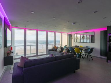 A living room and dining area with large windows overlooking the beach at Louies Loft in St Ives